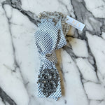 Load image into Gallery viewer, Black and white patterned tie with embellished brooch on a black and white marble surface
