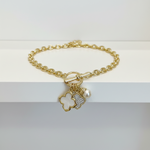 Load image into Gallery viewer, Gold-tone chain bracelet with a toggle clasp and three dangling charms: a white mother-of-pearl clover, a rhinestone-encrusted clover, and a white pearl, displayed on a white shelf.
