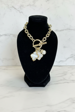 Load image into Gallery viewer, Gold-tone chain bracelet with a toggle clasp and three dangling charms: a white mother-of-pearl clover, a rhinestone-encrusted clover, and a white pearl, displayed on a black velvet jewelry bust.
