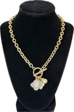 Load image into Gallery viewer, A gold chain necklace with a toggle clasp and a flower-shaped charm paved with clear stones and accented with a small pearl, displayed on a black velvet jewelry bust against a white background.
