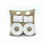Load image into Gallery viewer, A pair of chunky white statement earrings displayed on a woven burlap cushion.  The earrings feature a mix of geometric and organic shapes, including two round studs, two rectangular plates, and two large circular disc earrings with concentric ring detailing.
