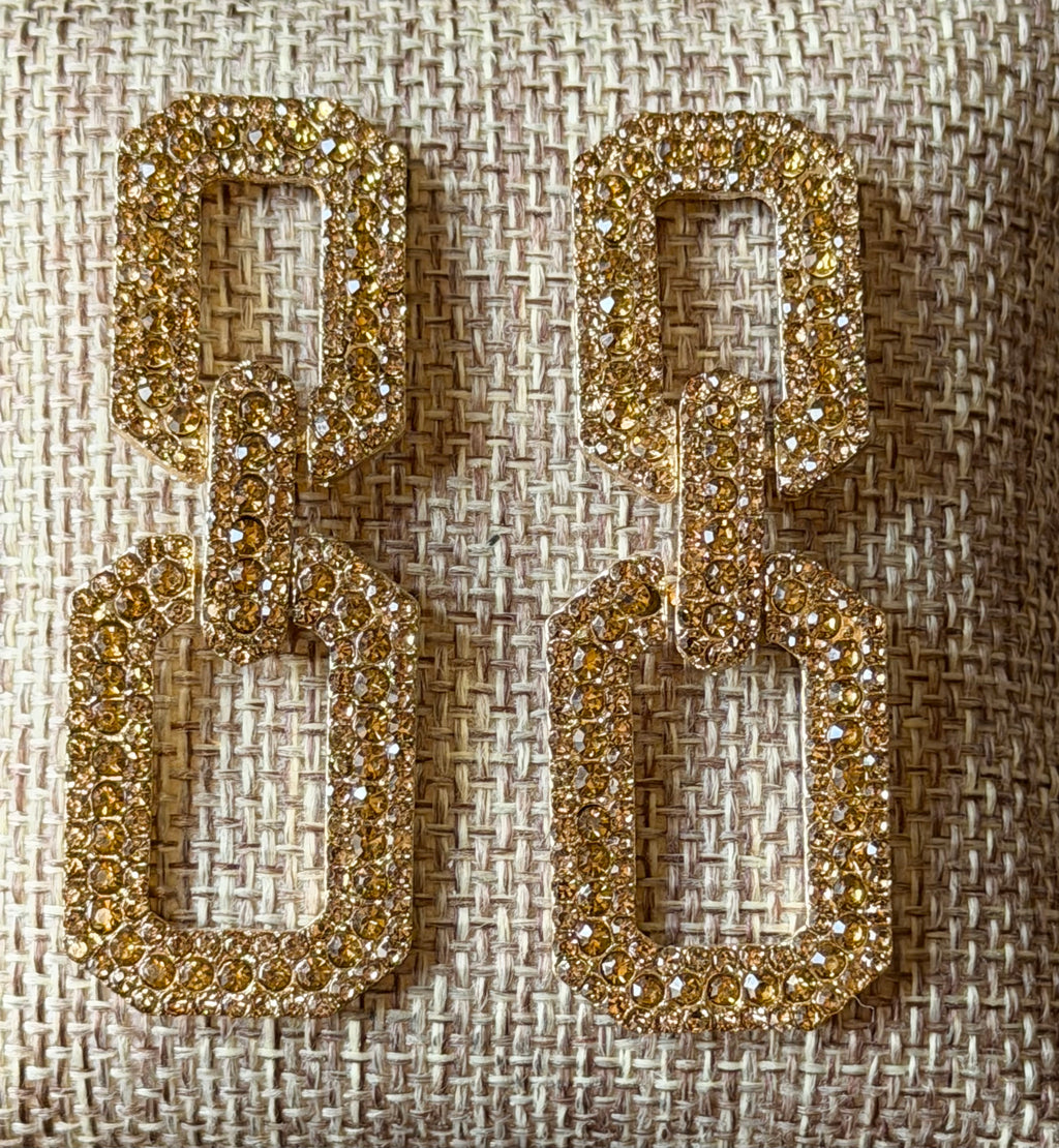 Gold rectangular earrings on a textured beige background