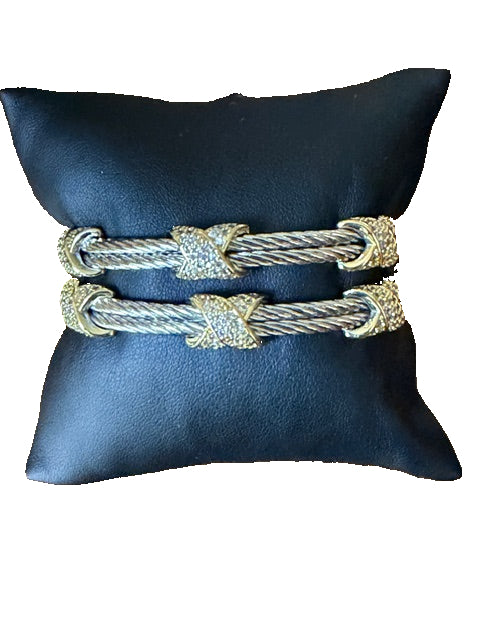 Pair of gold and silver cable-style bracelets on a black cushion 