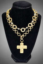 Load image into Gallery viewer, A gold-toned multi-strand chain necklace with a textured cross pendant, displayed on a black velvet jewelry bust against a gray ombre background.
