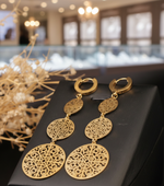 Load image into Gallery viewer, Gold earrings with intricate designs on a black surface with dried flowers.
