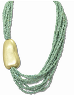Load image into Gallery viewer, A multi-strand statement necklace featuring light sage green square beads and a large, smooth, polished gold-colored pendant, shown against a plain white background.
