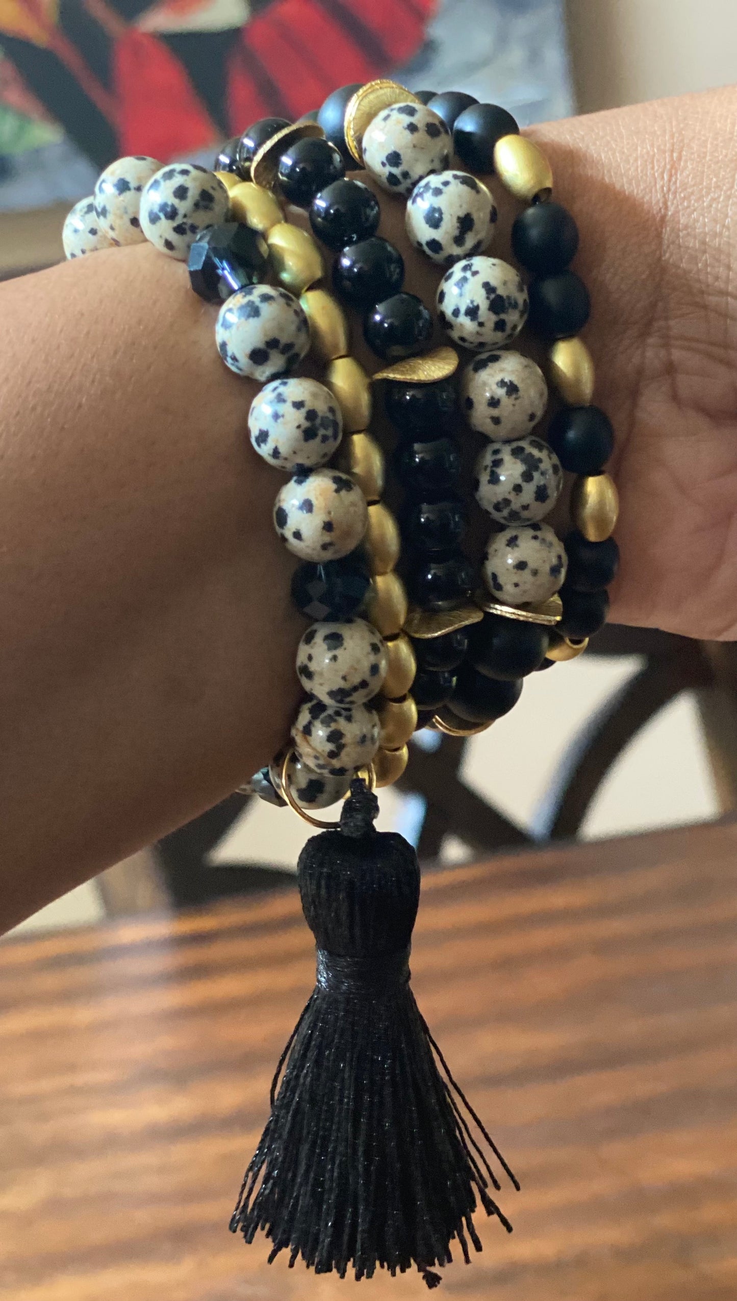 5 stretch bracelets with round Dalmatian jasper beads, gold barrel beads and round onyx beads with black knit tassel, shown on outstretched arm to show details of bracelet stack 